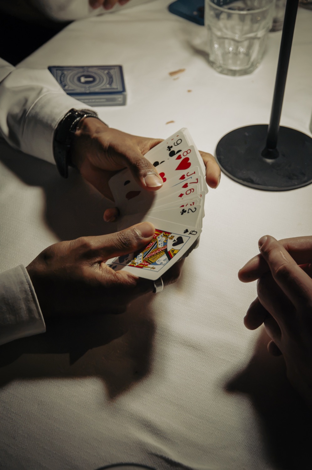 Hands fanning a deck of playing cards over a white tablecloth