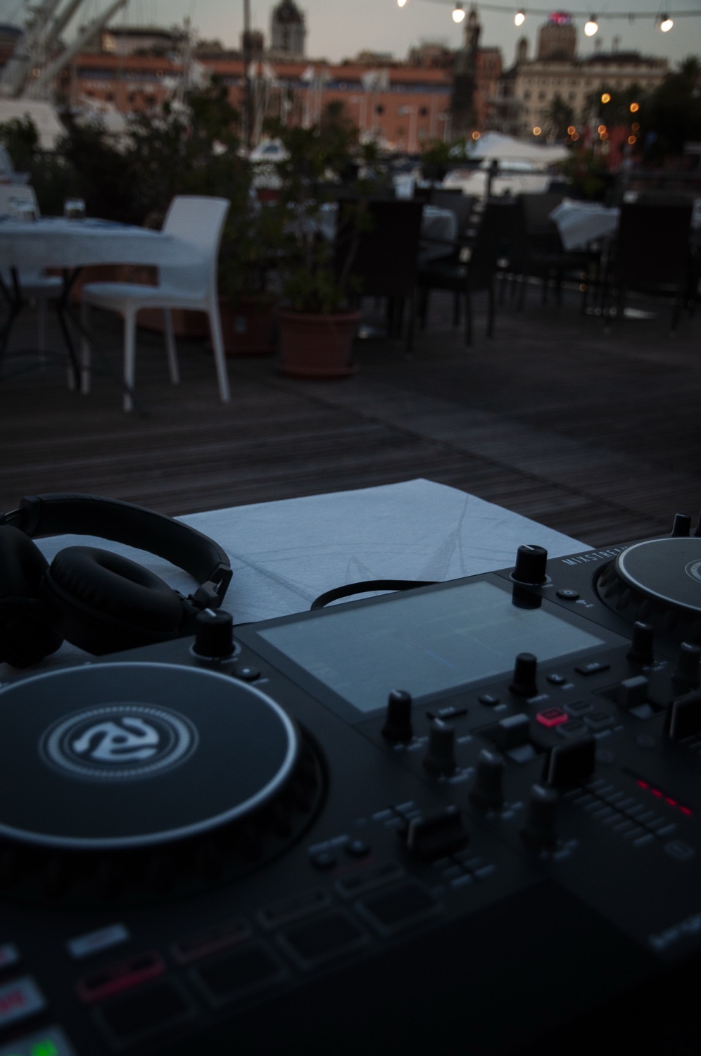 A DJ controller and headphones on a rooftop terrace at dusk, the city behind